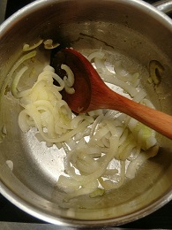 Sliced onions in a saucepan with a wooden spoon